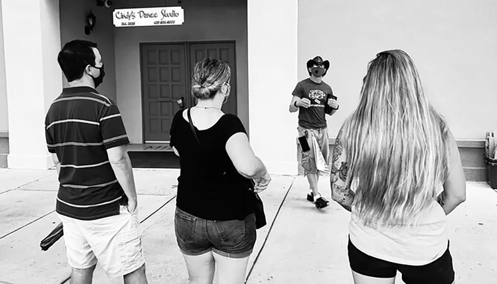Three people are standing on a sidewalk listening to a man who appears to be giving them instructions or information in front of a dance studio