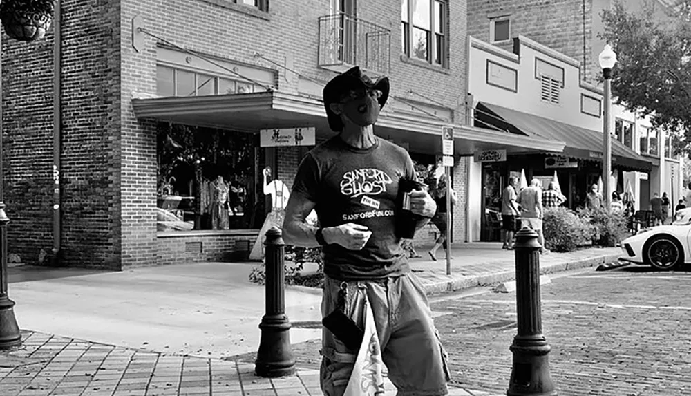 A person wearing a cowboy hat and sunglasses is standing on a sidewalk in an urban setting holding what appears to be a pamphlet or flyer while stores and pedestrians are visible in the background