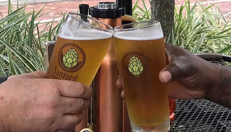 Two individuals are toasting with glasses of beer at an outdoor setting.
