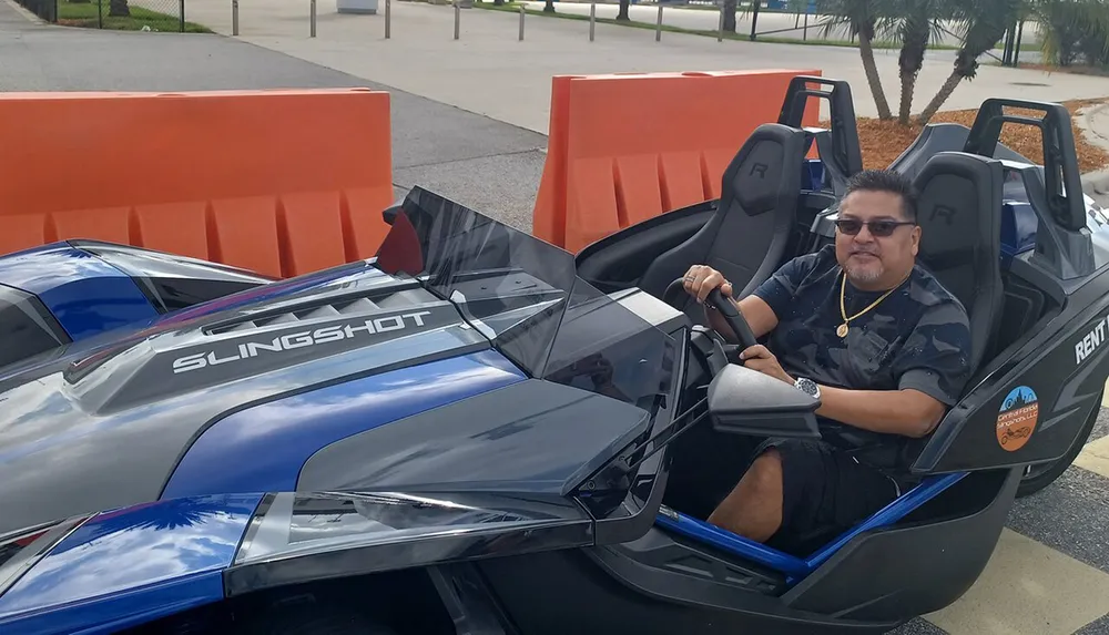 A person is seated in a parked Polaris Slingshot three-wheeled vehicle smiling and holding the steering wheel