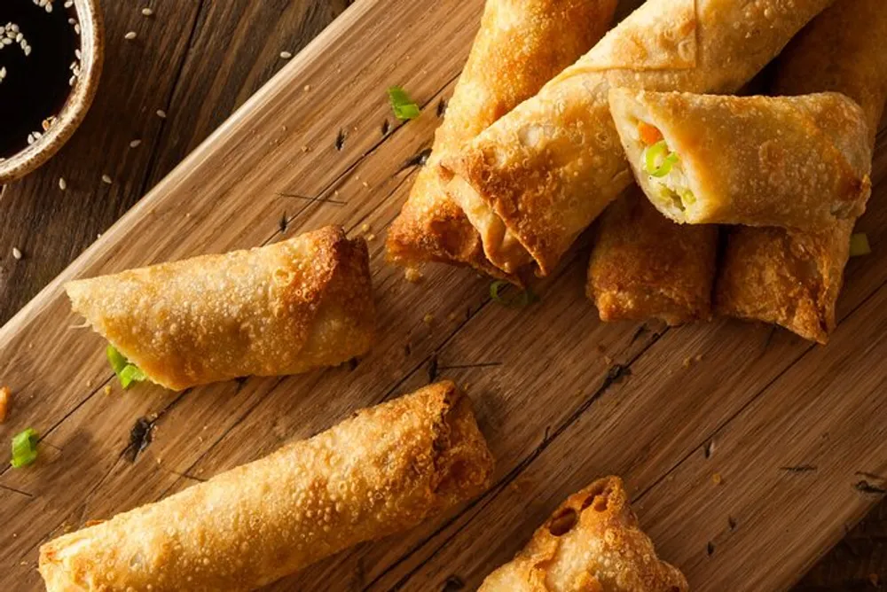 The image displays golden-brown fried spring rolls garnished with green onions on a wooden board suggesting an appetizing Asian-inspired dish