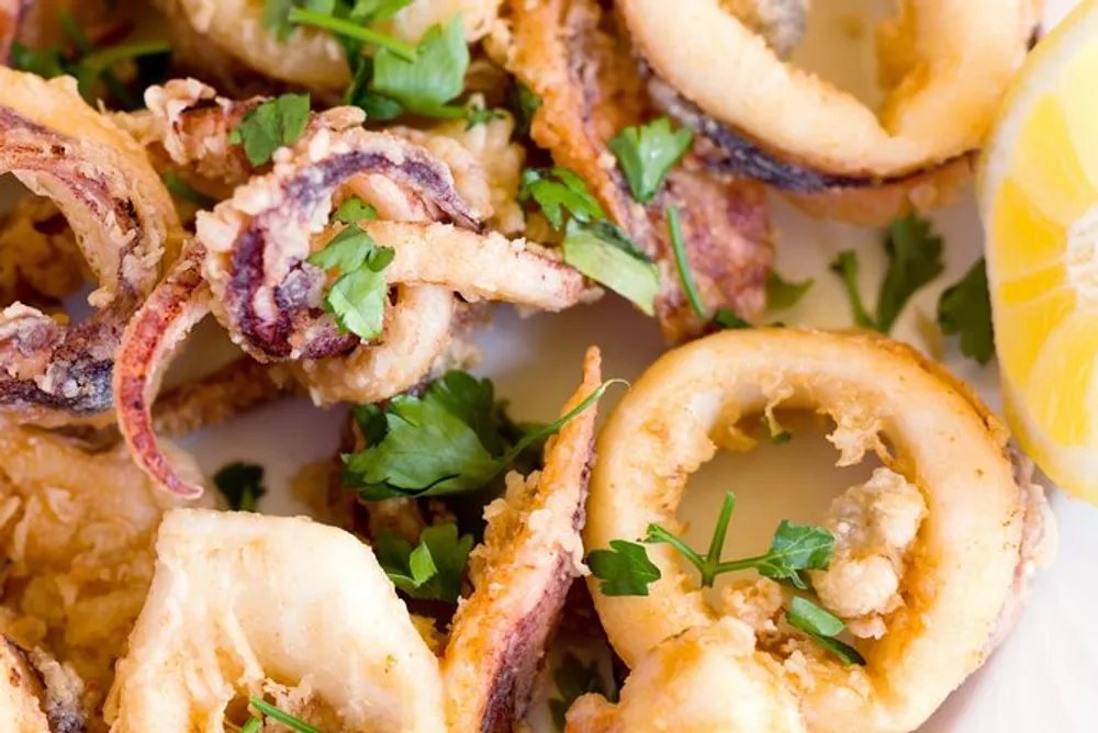 The image shows a close-up of crispy fried calamari garnished with parsley and accompanied by a slice of lemon