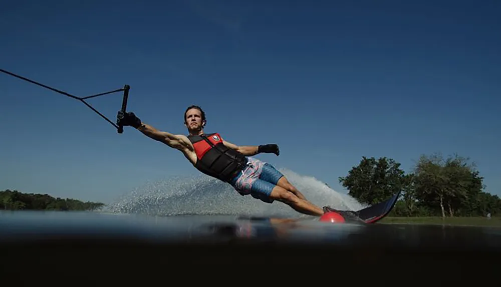 A person is water skiing leaning far to the side while holding onto a tow rope with a wake of water trailing behind and a clear blue sky above