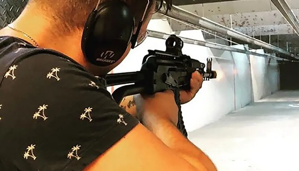 A person is aiming a rifle down a shooting range while wearing earmuffs for hearing protection
