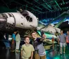Two boys take a selfie in front of the Space Shuttle Atlantis exhibit while other visitors explore the display