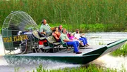 A group of people is enjoying a ride on a large airboat through a grassy wetland area.
