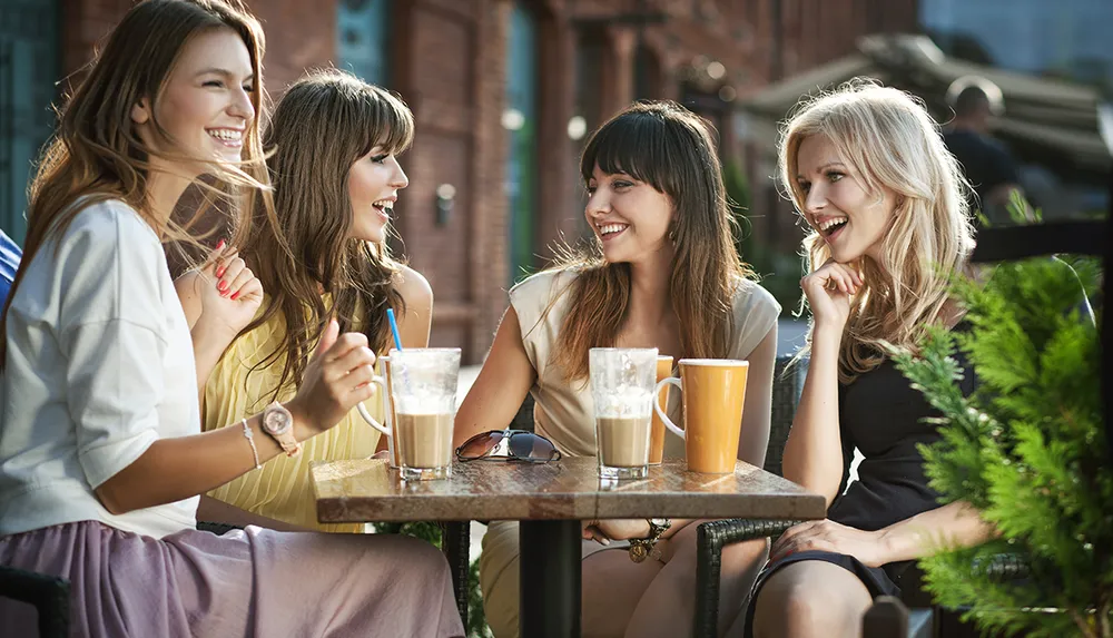 Four women are enjoying a lively conversation at an outdoor caf table with beverages