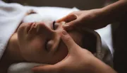 A person is receiving a relaxing facial massage, lying down with their eyes closed.