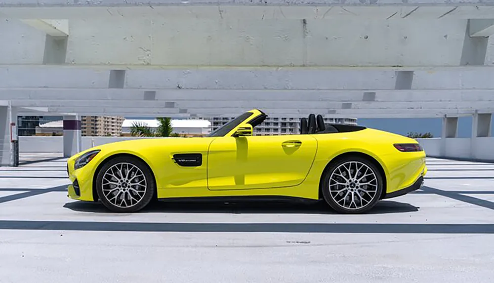 A bright yellow convertible sports car is parked in an empty parking garage under a clear blue sky