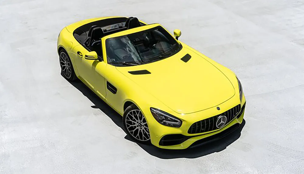 The image shows a bright yellow convertible Mercedes-Benz sports car parked on a flat concrete surface