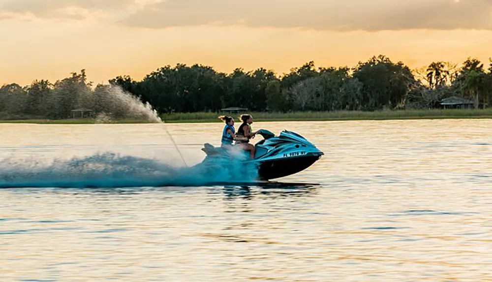 Two people are riding a personal watercraft at high speed on a water body during sunset