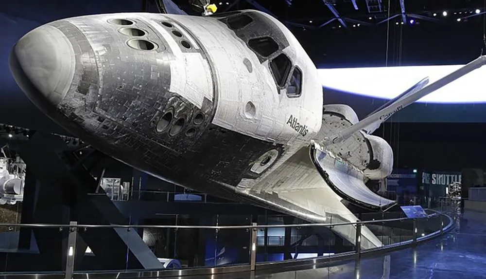 The image shows the Space Shuttle Atlantis displayed at a museum exhibit highlighting its detailed exterior and cargo bay doors open