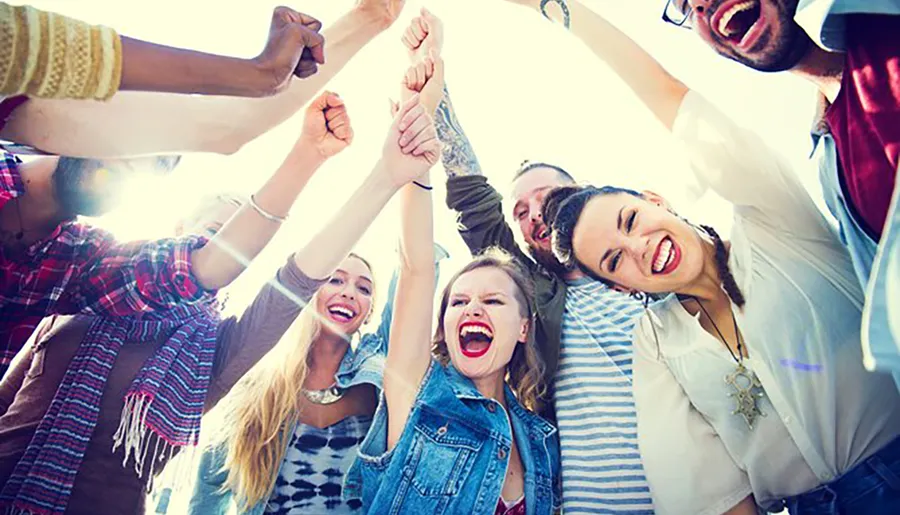 A group of joyful people are raising their arms together in a display of happiness and camaraderie under a sunny sky.