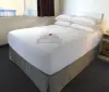 This image shows a neatly made bed with white linens in a simply furnished hotel room with a nightstand phone and a folded towel on the bed