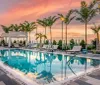 An outdoor swimming pool area with lounge chairs and palm trees during a vibrant sunset