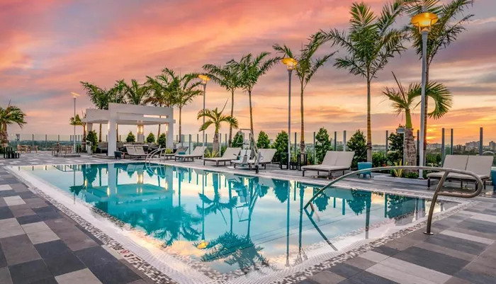 An outdoor swimming pool area with lounge chairs and palm trees during a vibrant sunset