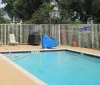 An outdoor swimming pool is surrounded by a metal fence with lounge chairs a grill covered with a tarp and a life ring mounted on the fence