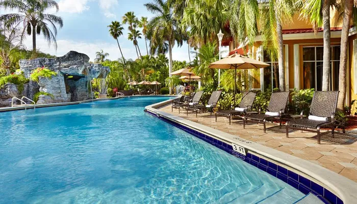 This is an inviting resort pool flanked by sun loungers and umbrellas featuring a rock waterfall and surrounded by tropical palm trees