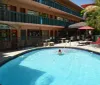 A person is enjoying a swim in an outdoor pool surrounded by a motel building with a restaurant nearby on a sunny day