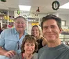 Four individuals are smiling for a selfie at a cafe or bakery with shelves stocked with goods and Christmas decorations in the background