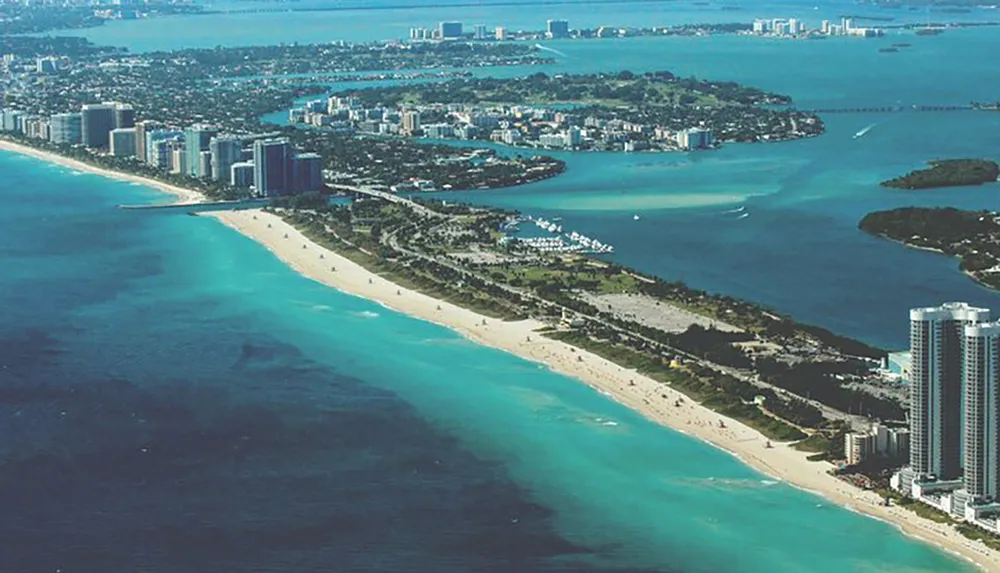 The image displays an aerial view of a coastal urban area with a long stretch of sandy beach clear blue waters and high-rise buildings along the shore