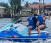 Two individuals are riding jet skis on the water near a docked replica of an old sailing ship