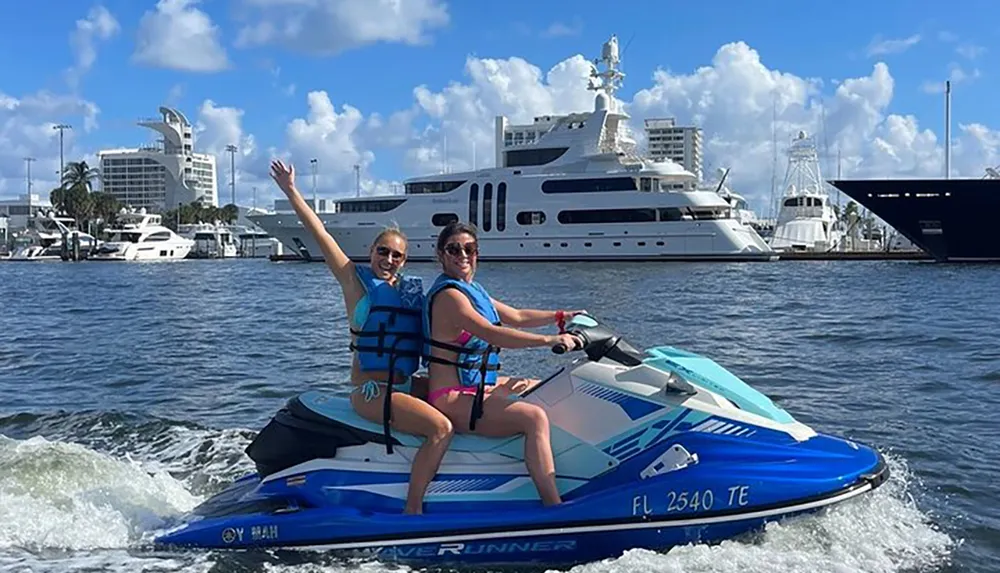 Two people are riding a jet ski with arms raised in celebration against a backdrop of yachts and water under a partly cloudy sky