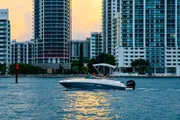 The image captures a motorboat cruising on the water near an urban skyline during sunset, with the sun's reflection on the water.