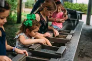 Children are engrossed in gemstone mining at a water-filled sluice with wooden trays.