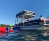 A pontoon boat with passengers is cruising near a lush shoreline under bright sunlight