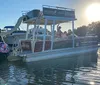 A pontoon boat with passengers is cruising near a lush shoreline under bright sunlight