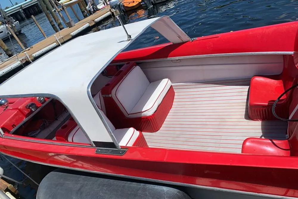 The image shows a close-up of a red and white open motorboat tied to a dock on a sunny day
