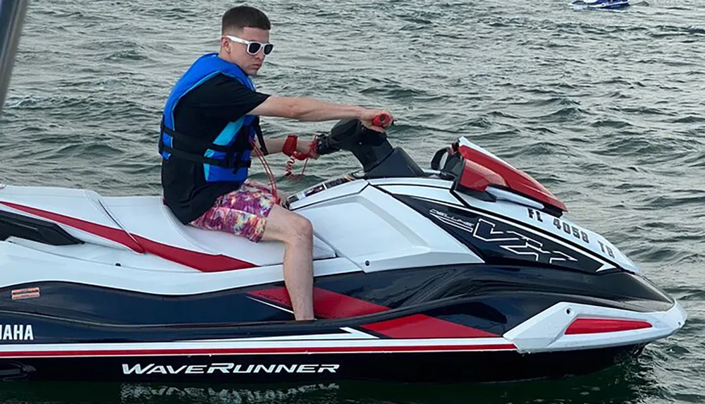 A person in sunglasses and a life vest is riding on a Yamaha WaveRunner personal watercraft on the water