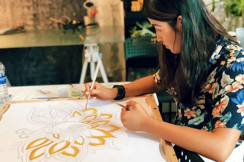 A person is intricately painting a large mandala design on fabric