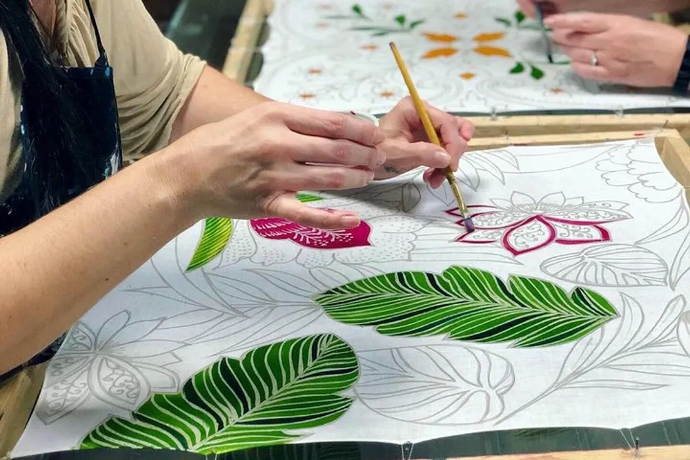 A person is hand-painting a colorful floral pattern on fabric