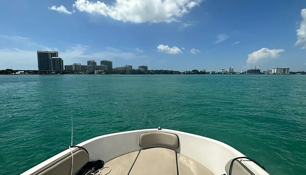 A boat is heading towards a coastline dotted with buildings under a clear blue sky