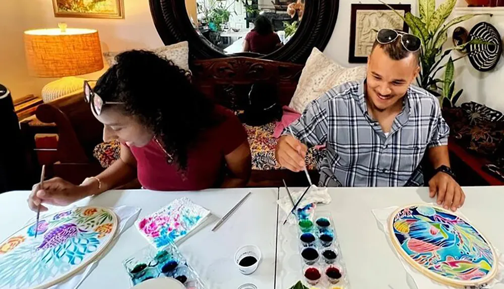 Two people are happily engaged in creating colorful silk paintings at a well-lit arts and crafts table