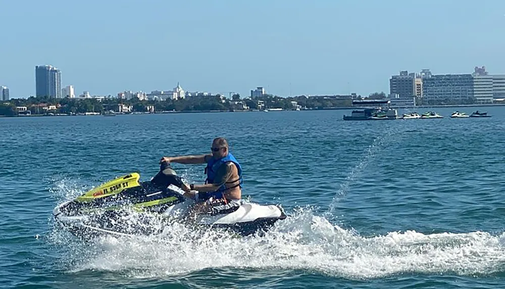 A person is riding a jet ski across a body of water with a city skyline in the background