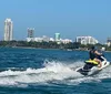 A person is riding a jet ski across a body of water with a city skyline in the background