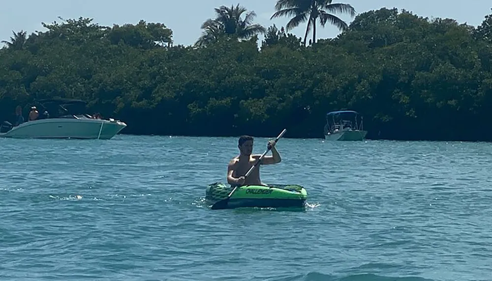 A person is paddling a bright green inflatable kayak on a sunny day with motorboats and greenery in the background