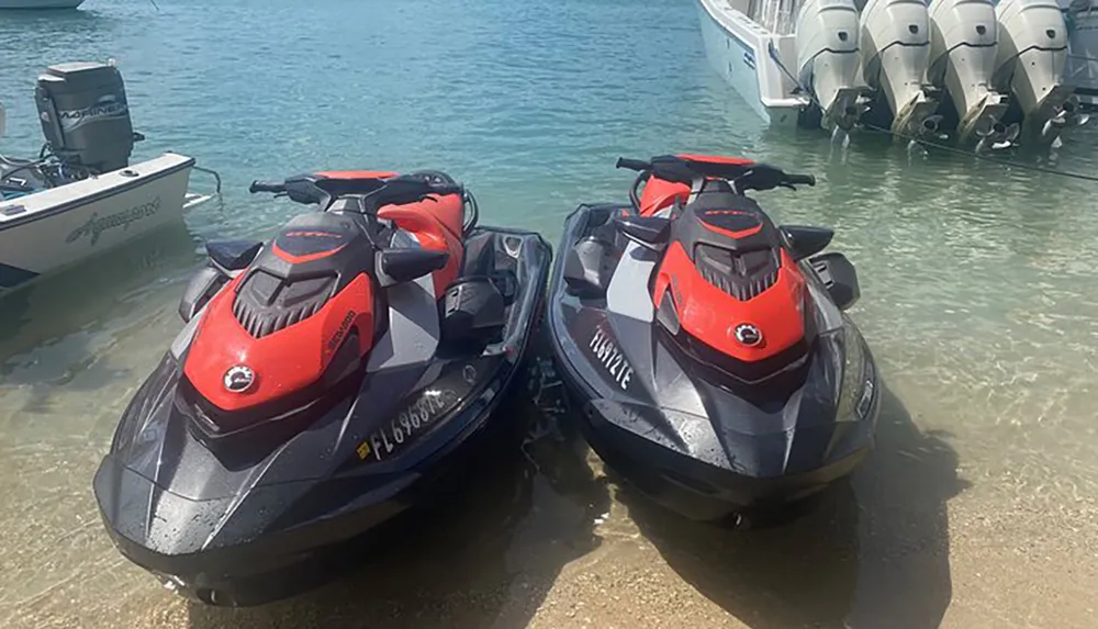 Two jet skis are parked in shallow waters near a boat equipped with multiple outboard engines on a sunny day