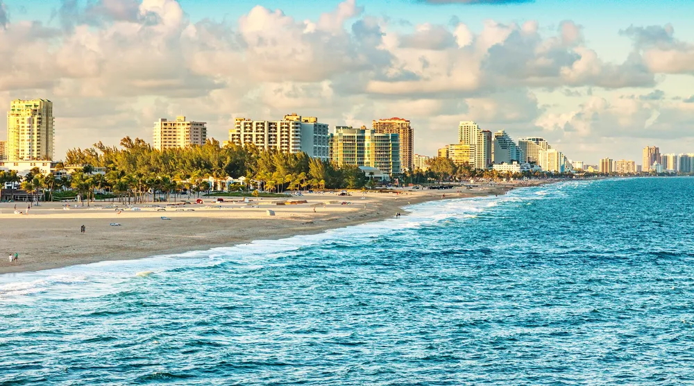 The image features a coastal cityscape with high-rise buildings along a sunlit beach flanked by the blue ocean