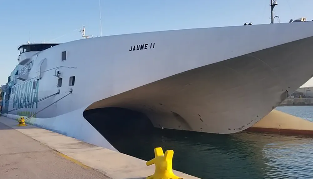 The image shows the bow of a large white ship named JAUME II docked at a quay next to a yellow bollard