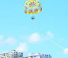 Two people are enjoying a parasailing adventure in a clear blue sky with a vibrant pink parachute above them