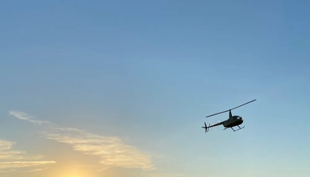 A helicopter is flying in a clear sky with the setting sun in the background