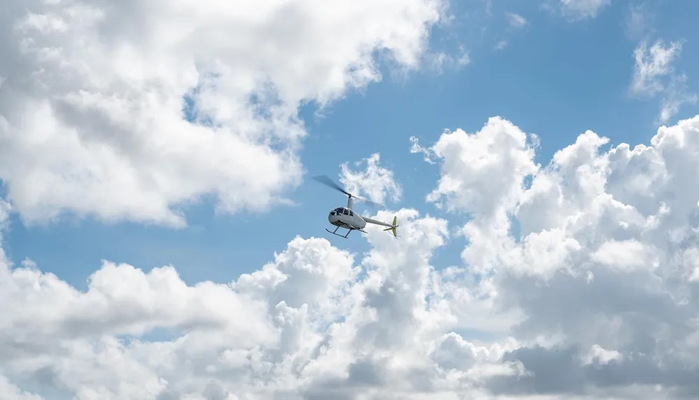 A helicopter is flying against a backdrop of white fluffy clouds in a blue sky