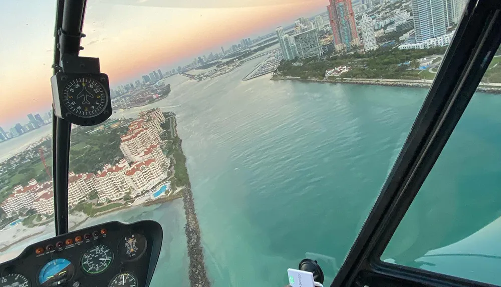 The image shows an aerial view of a coastal cityscape at dusk from the cockpit of a helicopter