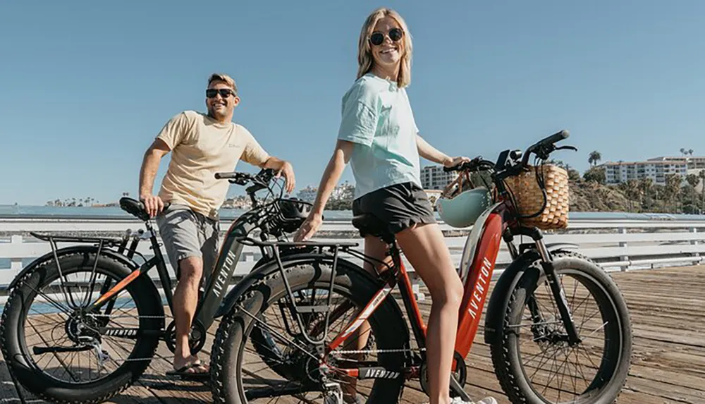 A man and a woman are smiling and posing with their bicycles on a sunny pier suggesting a leisurely day out