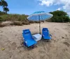 A relaxing beach setup featuring two blue lounge chairs and a cooler under a patterned umbrella on sandy shore