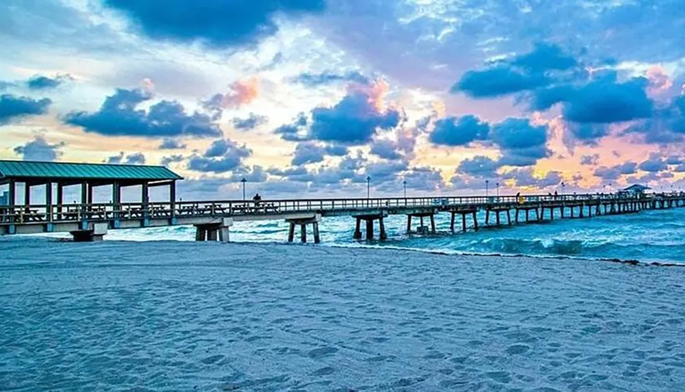 A vibrant sky with hues of blue and pink looms over a serene beach and a wooden pier extending into the sea